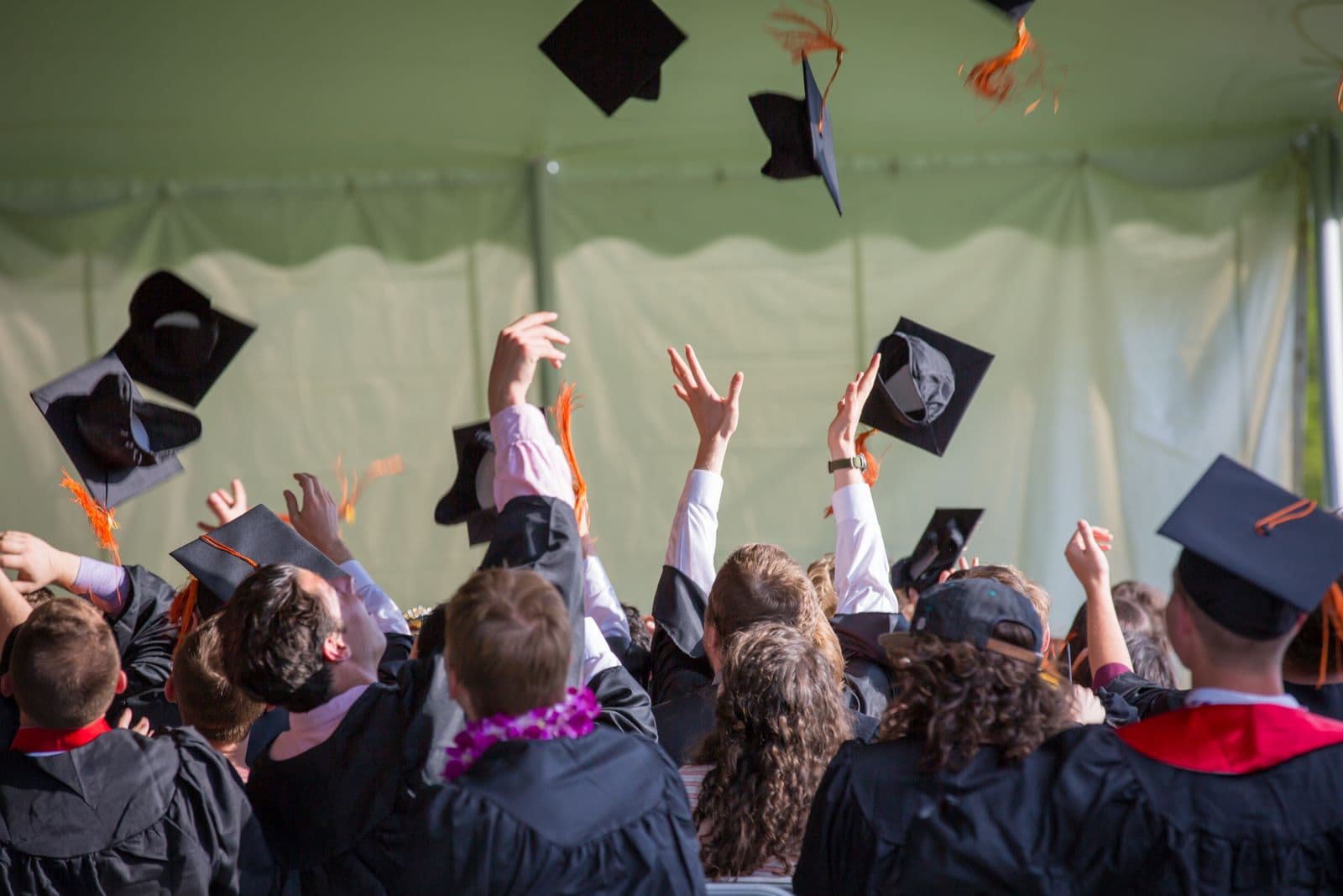 Graduates raising their hands as caps fly overhead